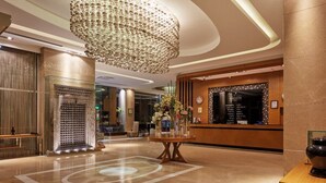 Een moderne lobby met een grote kroonluchter, een receptiebalie en een decoratief vloerpatroon.