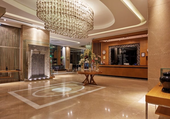 A modern lobby with a large chandelier, a reception desk, and a decorative floor pattern.