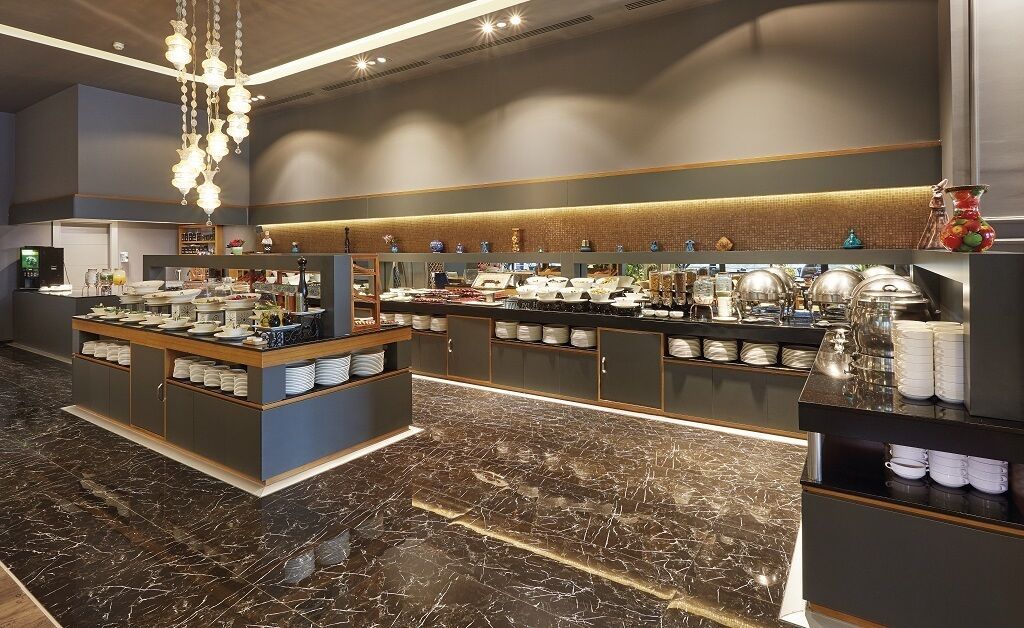 A modern hotel lobby with marble flooring, a central buffet area, and a variety of amenities including a coffee station and decorative items.