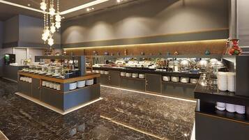 A modern hotel lobby with marble flooring, a central buffet area, and a variety of amenities including a coffee station and decorative items.