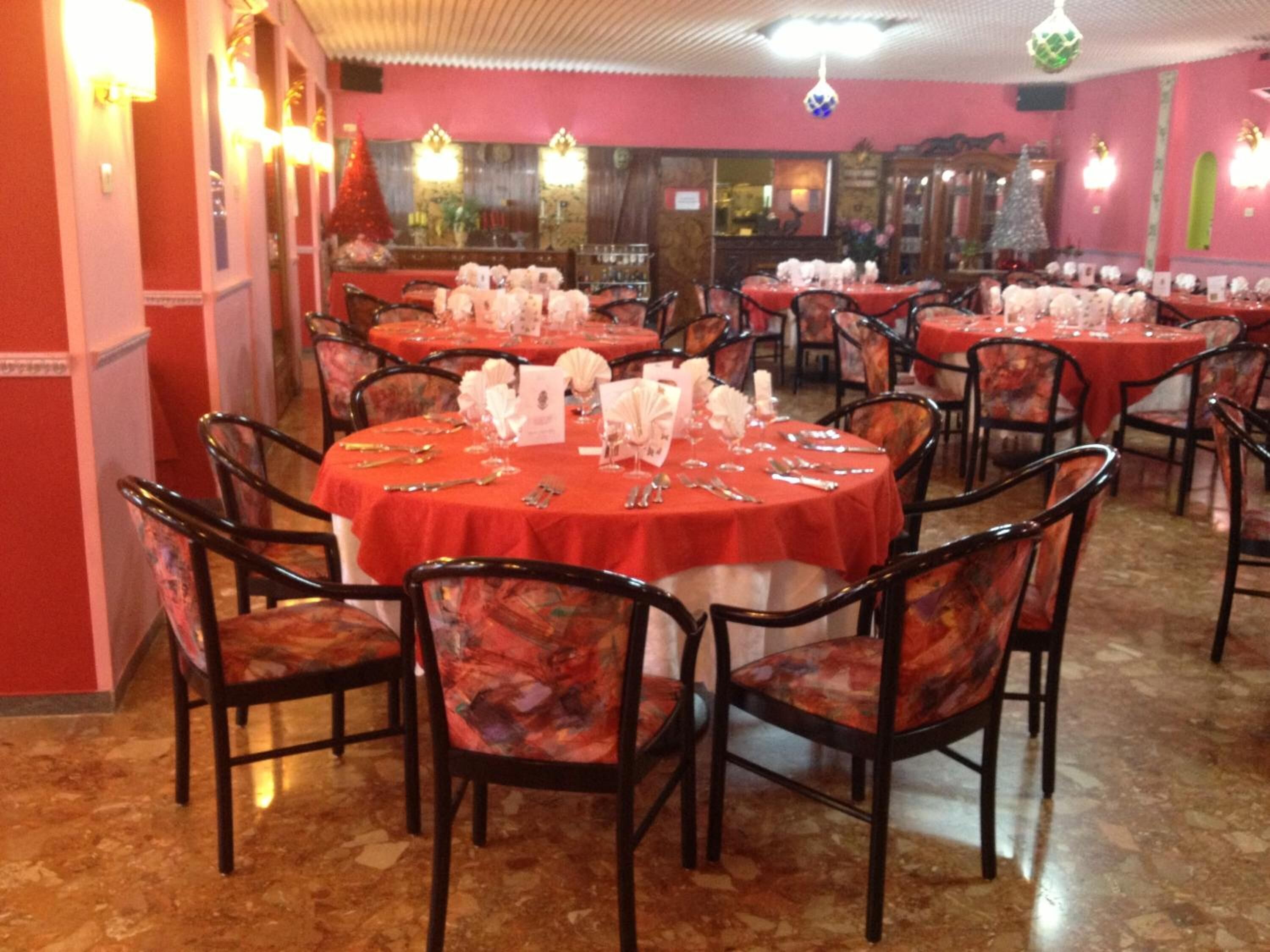 Un restaurant avec des tables rondes recouvertes de nappes rouges, des chaises noires et une vaisselle blanche.