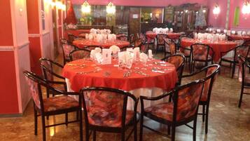 Un restaurant avec des tables rondes recouvertes de nappes rouges, des chaises noires et une vaisselle blanche.