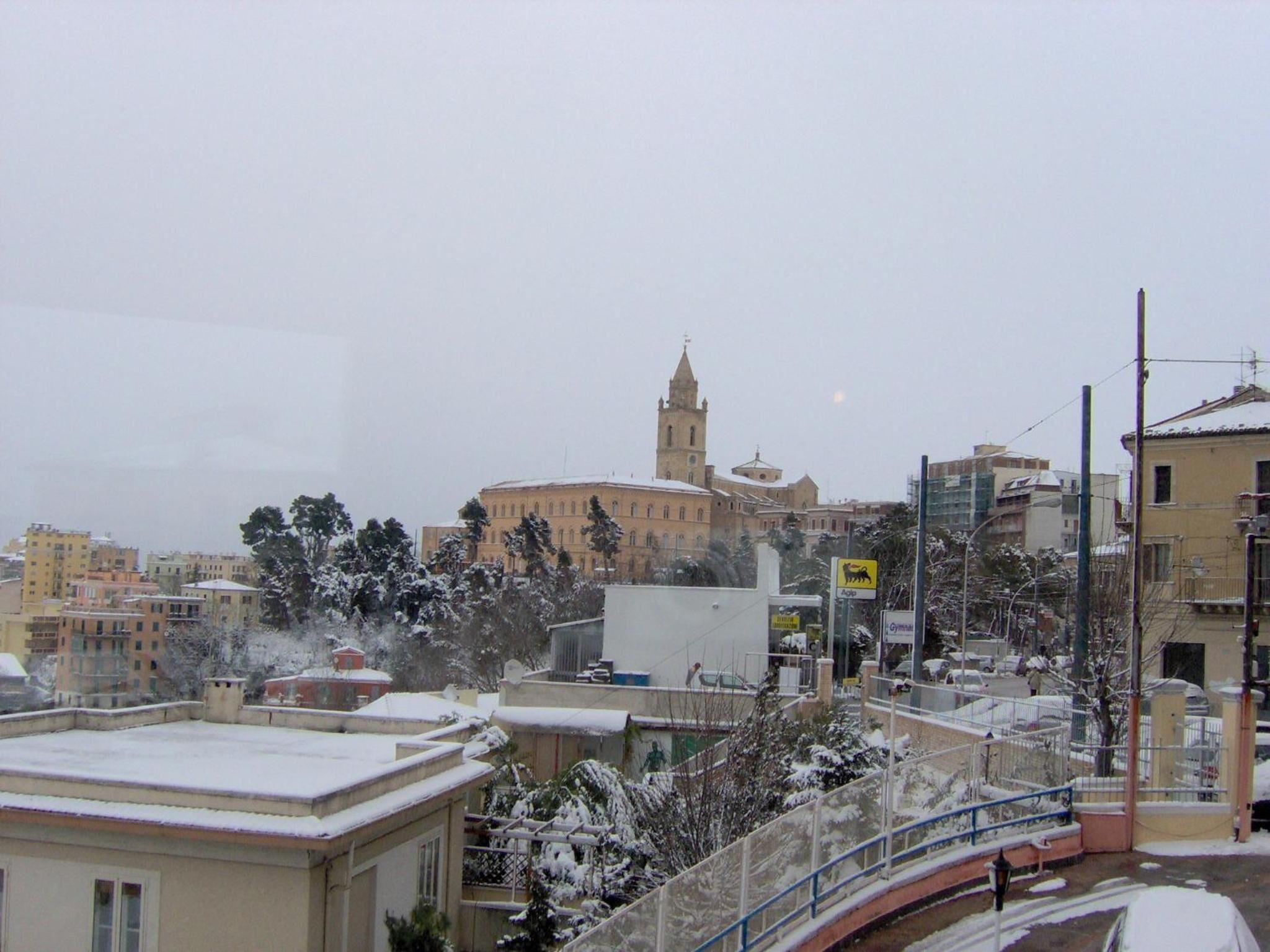 Un paisaje urbano nevado con un edificio destacado que tiene una torre, rodeado de edificios residenciales y un puente.