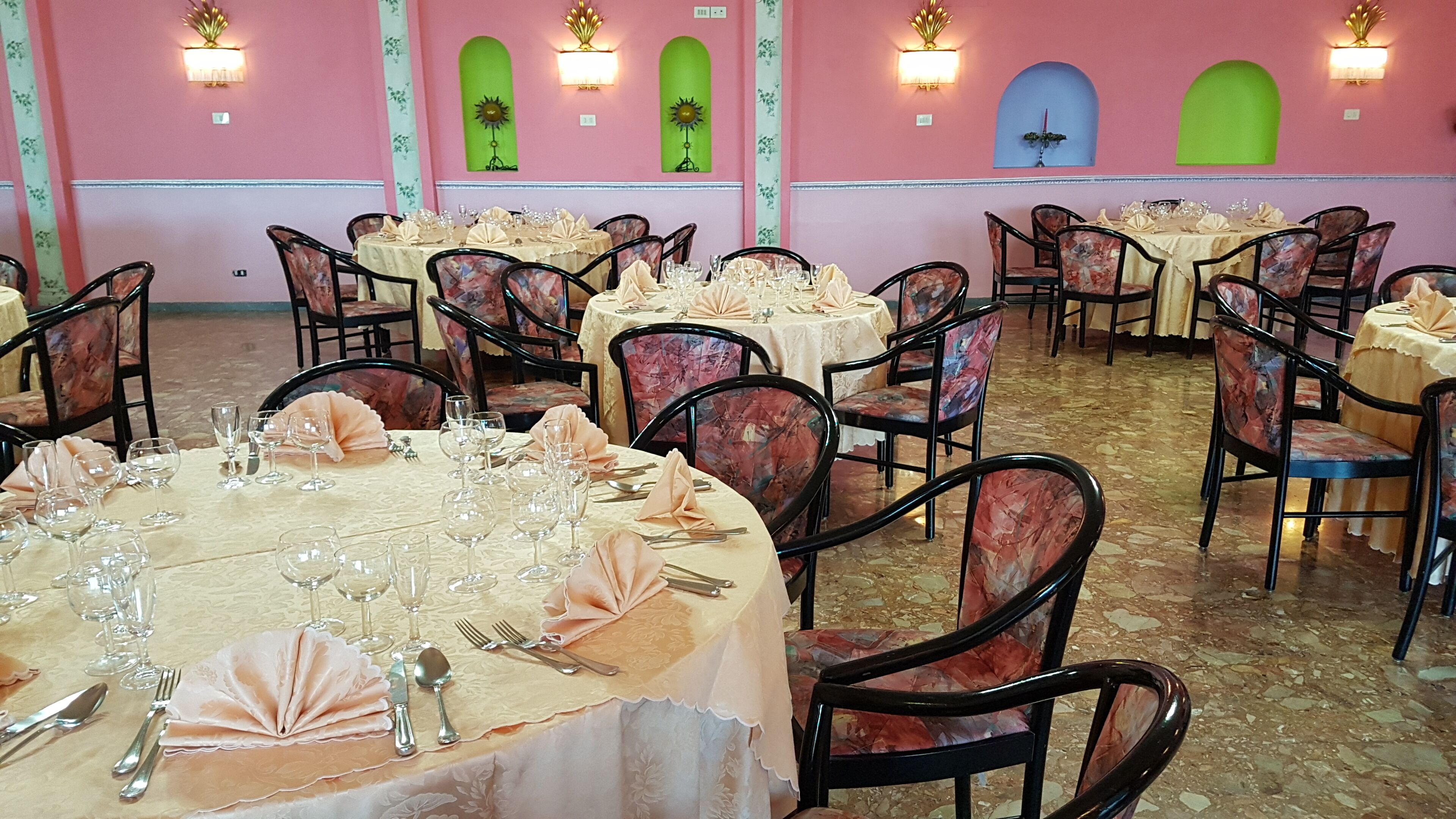 A dining area with round tables set for a meal, surrounded by chairs with floral upholstery.