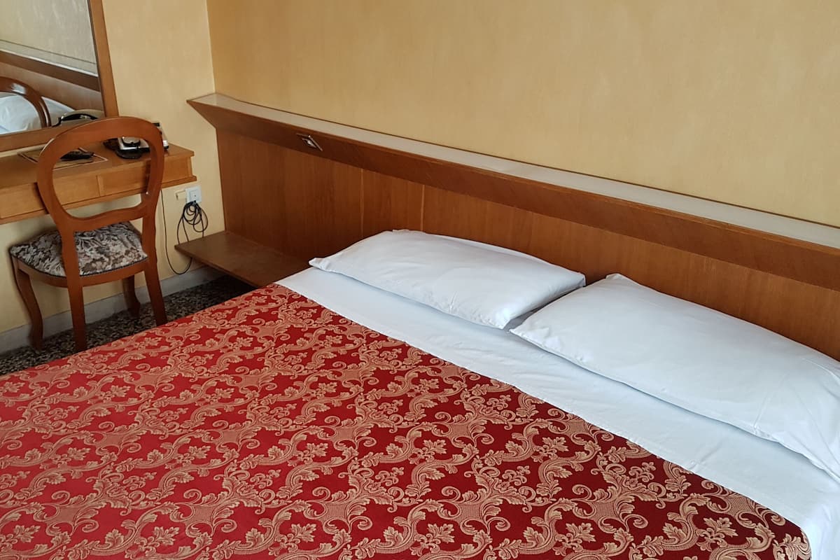 A hotel room with a bed, a desk with a chair, and a mirror.