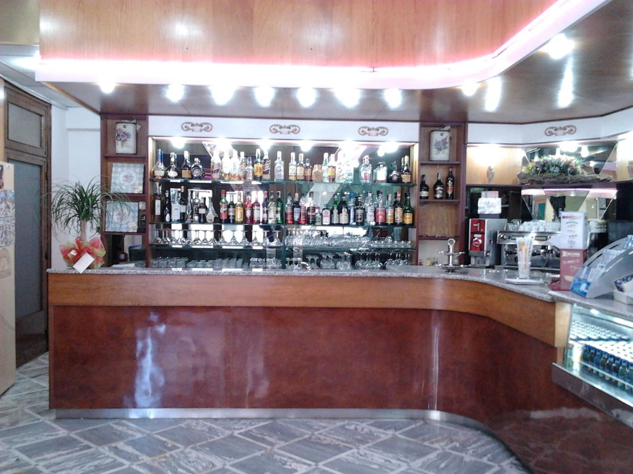 A bar area with a curved counter, shelves with various bottles, glasses, and a cash register.