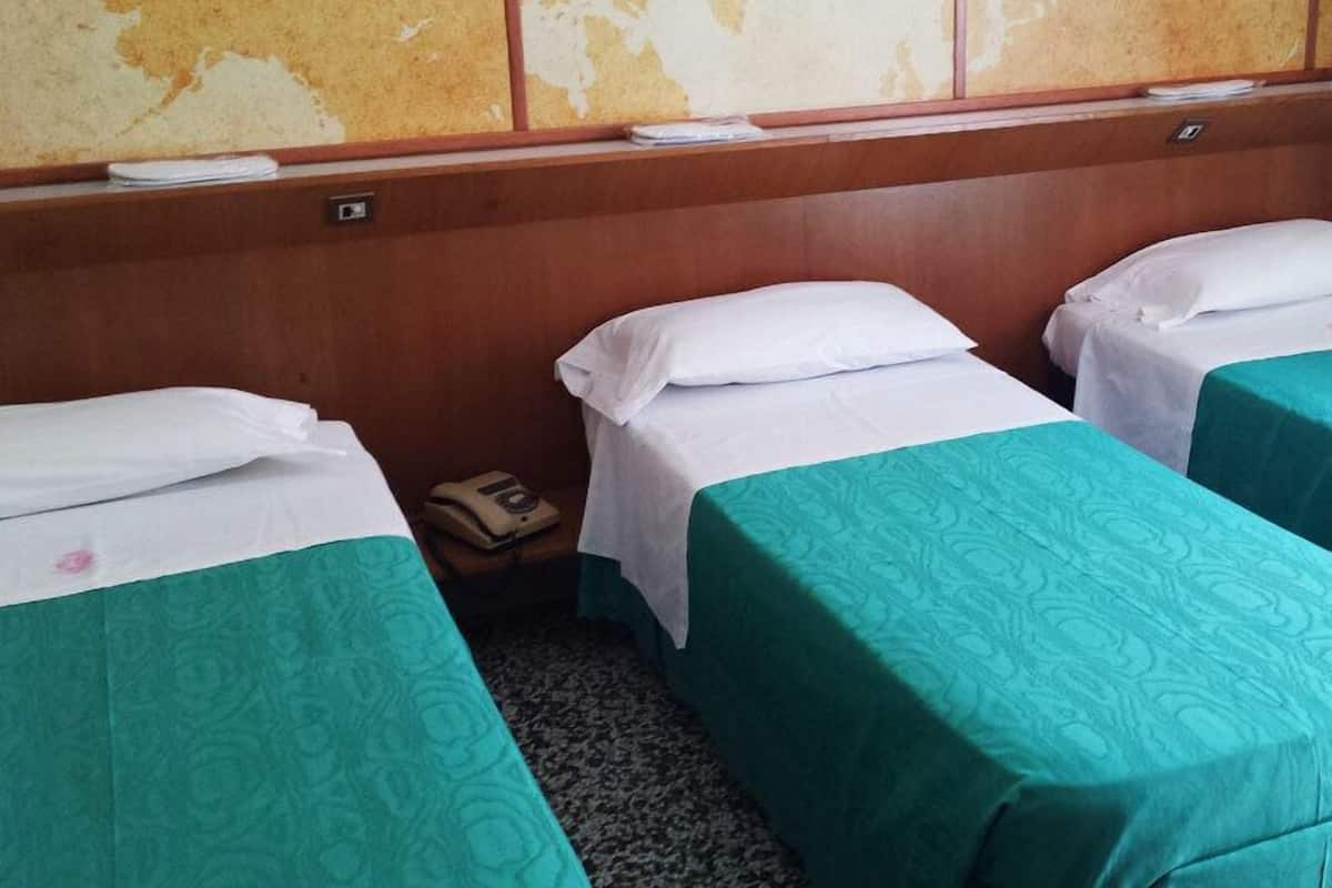 A hotel room with three single beds, each with a green bedspread and white pillows. The room has a wooden headboard and a wall with a map design.