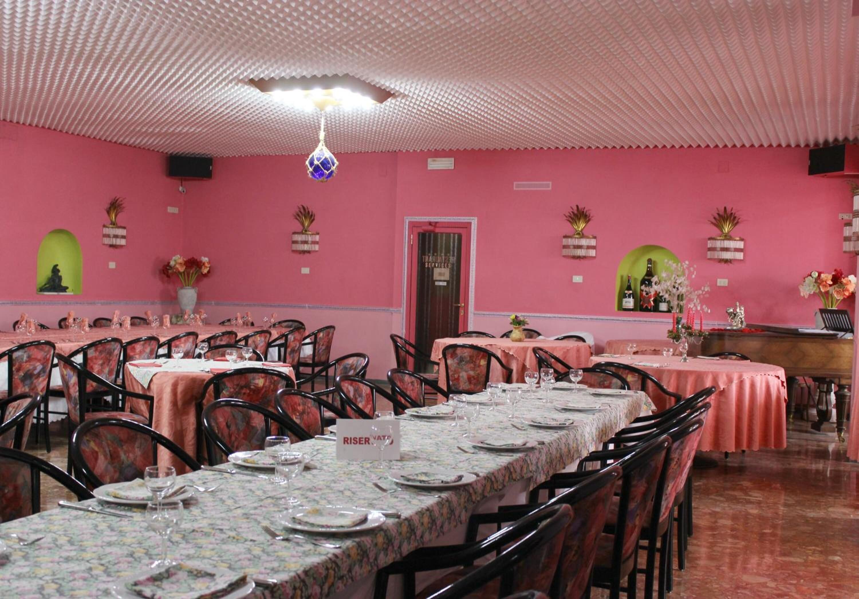 A dining area with pink walls, tables set with plates and glasses, and chairs.