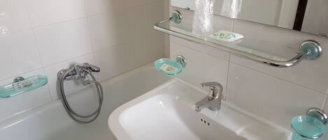 A bathroom with a white sink, a glass shower enclosure, and a glass shelf with toiletries.