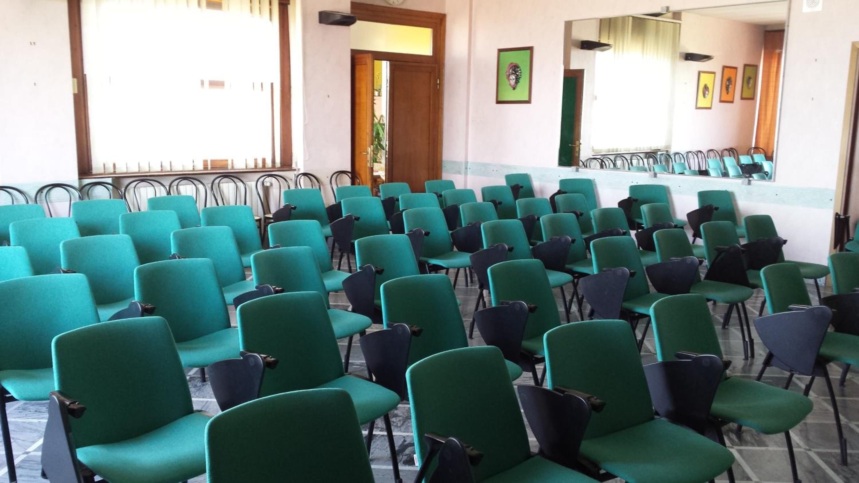 A conference room with rows of teal chairs and a long table at the front.