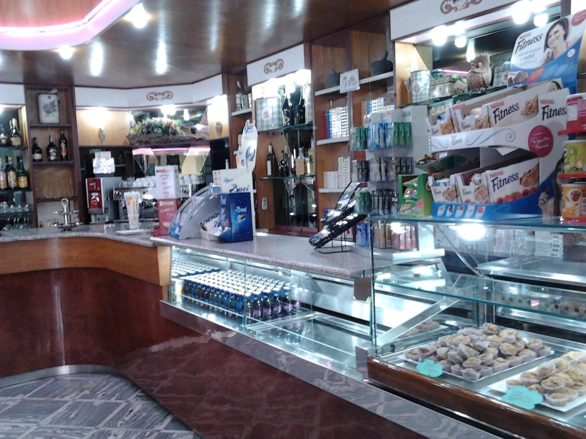Mostrador de panadería con pasteles y una zona de cafetería con diversas bebidas y aperitivos.