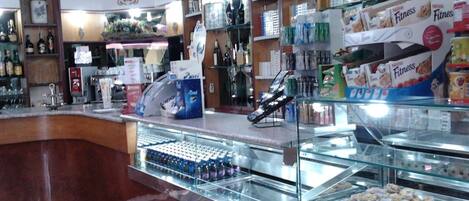 Mostrador de panadería con pasteles y una zona de cafetería con diversas bebidas y aperitivos.