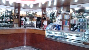 A bar area with a curved counter, shelves with bottles, and a display of bottled water. - Grande Albergo Abruzzo (Chieti)