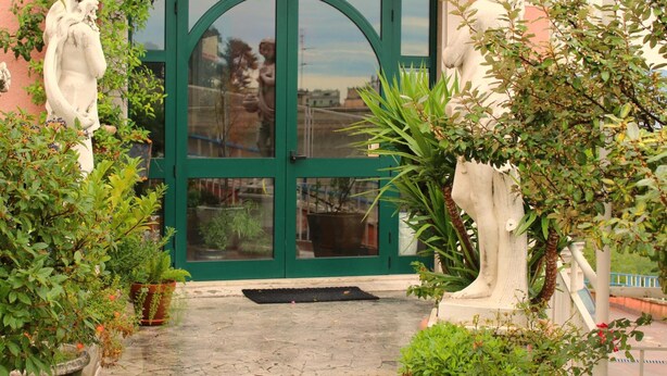 A restaurant entrance with a green door, two stone statues on either side, and potted plants in the foreground. - Grande Albergo Abruzzo (Chieti)