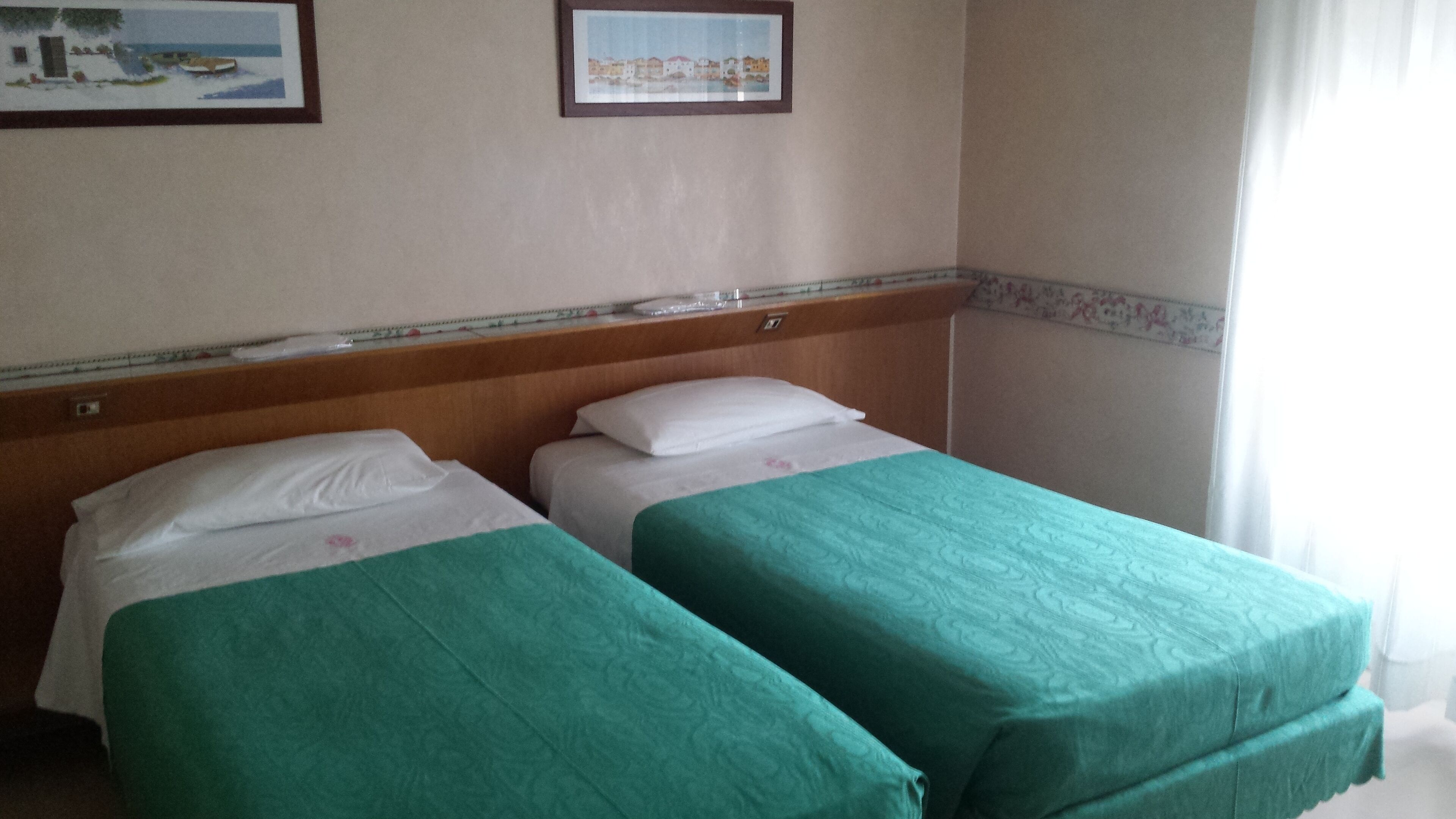 Ein Hotelzimmer mit zwei Einzelbetten, Holz-Kopfteilen, einem kleinen Tisch und einem gerahmten Bild an der Wand.