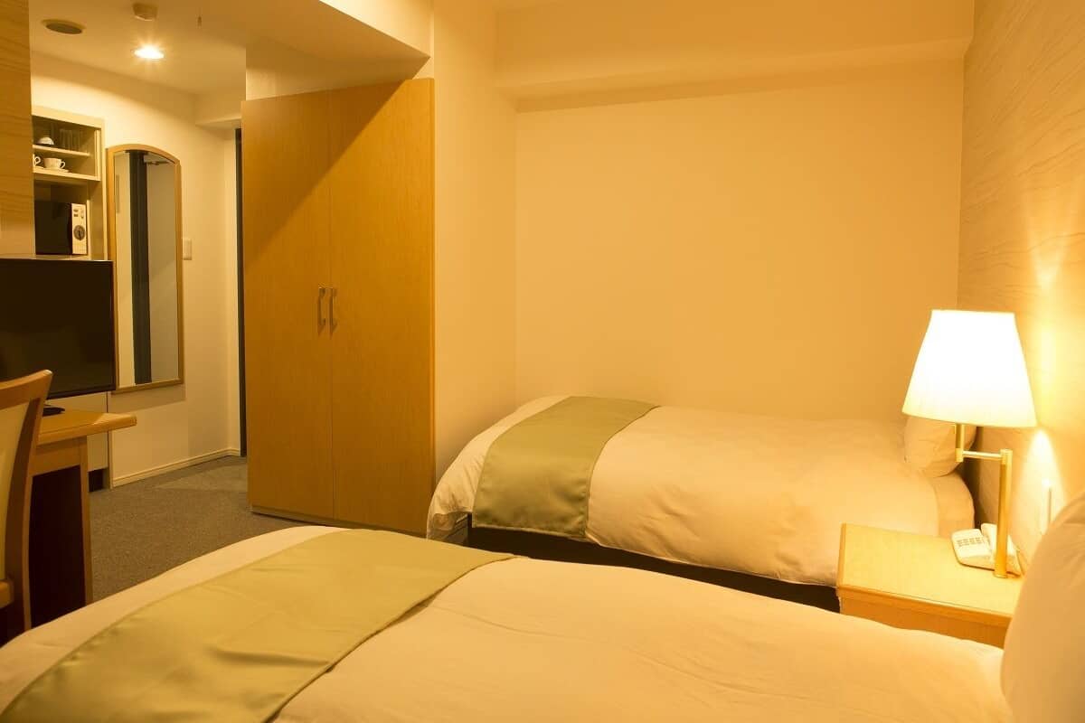 Ein Hotelzimmer mit zwei Betten, einem Schreibtisch, einem Stuhl, einem Kleiderschrank und einer Lampe.