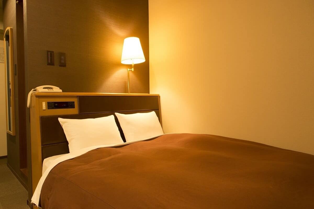 Ein Hotelzimmer mit einem Bett, einer Lampe, einem Telefon und einem an der Wand befestigten Lichtschalter.
