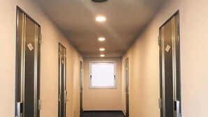 A corridor with doors on both sides, a window at the end, and a ceiling light. - Nissin Namba Inn (Osaka)