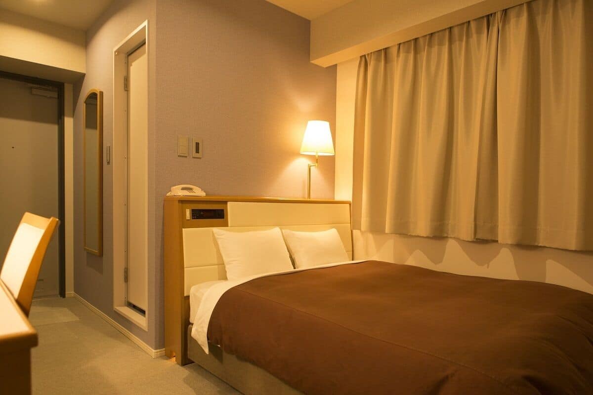 Ein Hotelzimmer mit einem Bett, einer Nachttischlampe, einem Stuhl und einer Tür.
