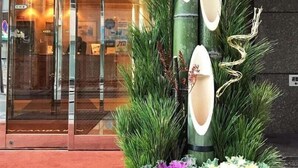 A hotel entrance with a glass door, a vertical arrangement of green plants, and a wooden planter with various leafy plants. - Nissin Namba Inn (Osaka)