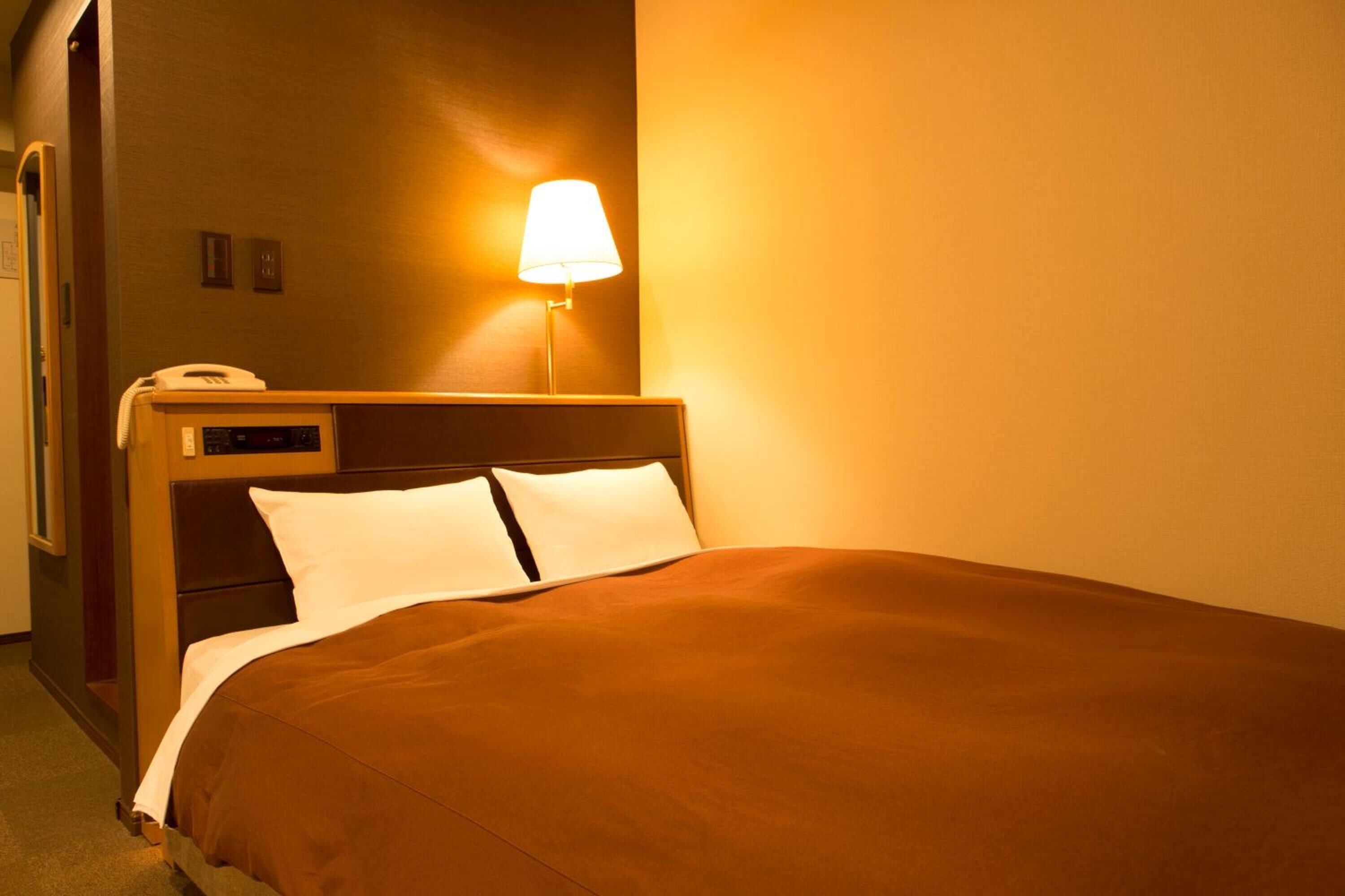 A hotel room with a bed, a bedside lamp, and a telephone.