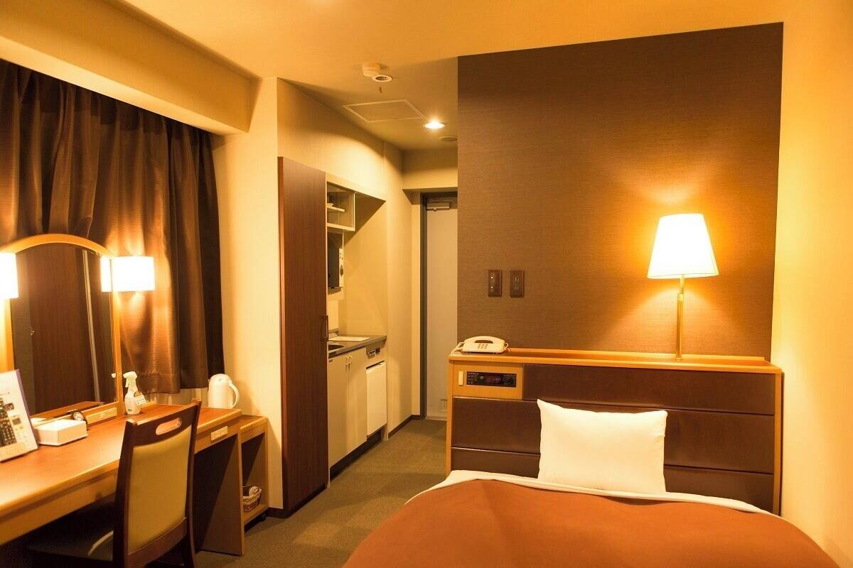 Ein Hotelzimmer mit Bett, Schreibtisch, Stuhl, Lampe und einer Küchenzeile.