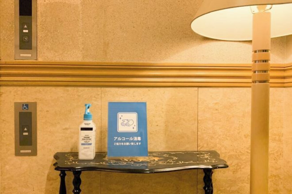 A hotel lobby with a reception desk, a hand sanitizer dispenser, and a sign indicating a handwashing station.