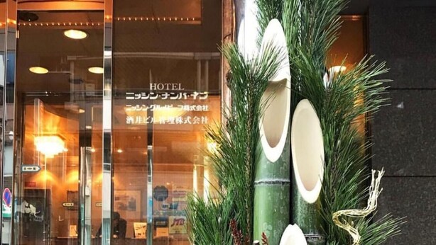 A hotel entrance with a glass door, a reception desk, and a decorative plant arrangement. - Nissin Namba Inn (Osaka)