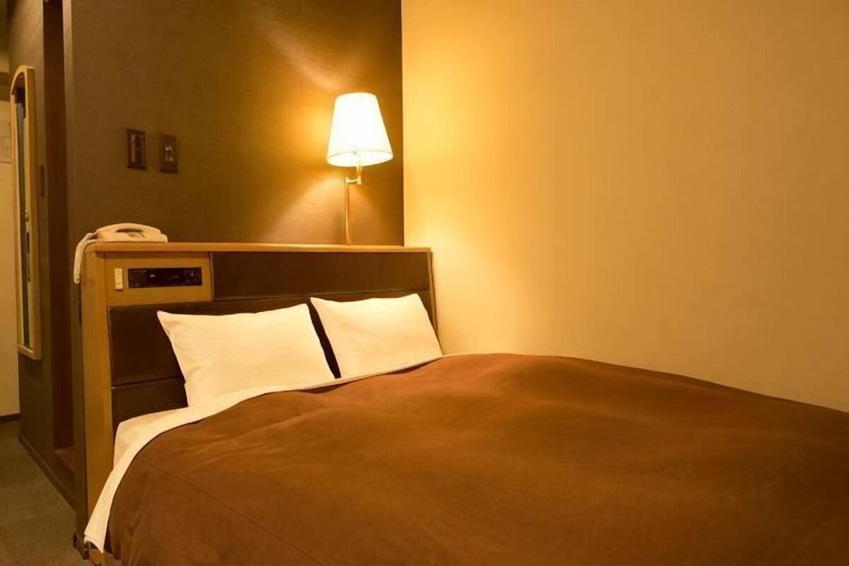 A hotel room with a bed, a bedside lamp, and a telephone.