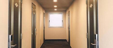 A narrow, well-lit hallway with a window at the end, flanked by doors on both sides.