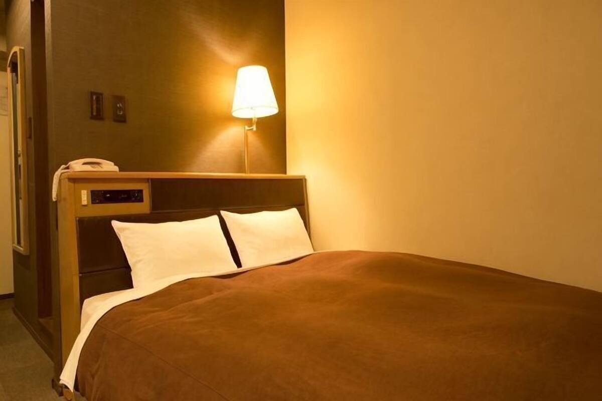 A hotel room with a bed, a bedside lamp, and a telephone on the nightstand.