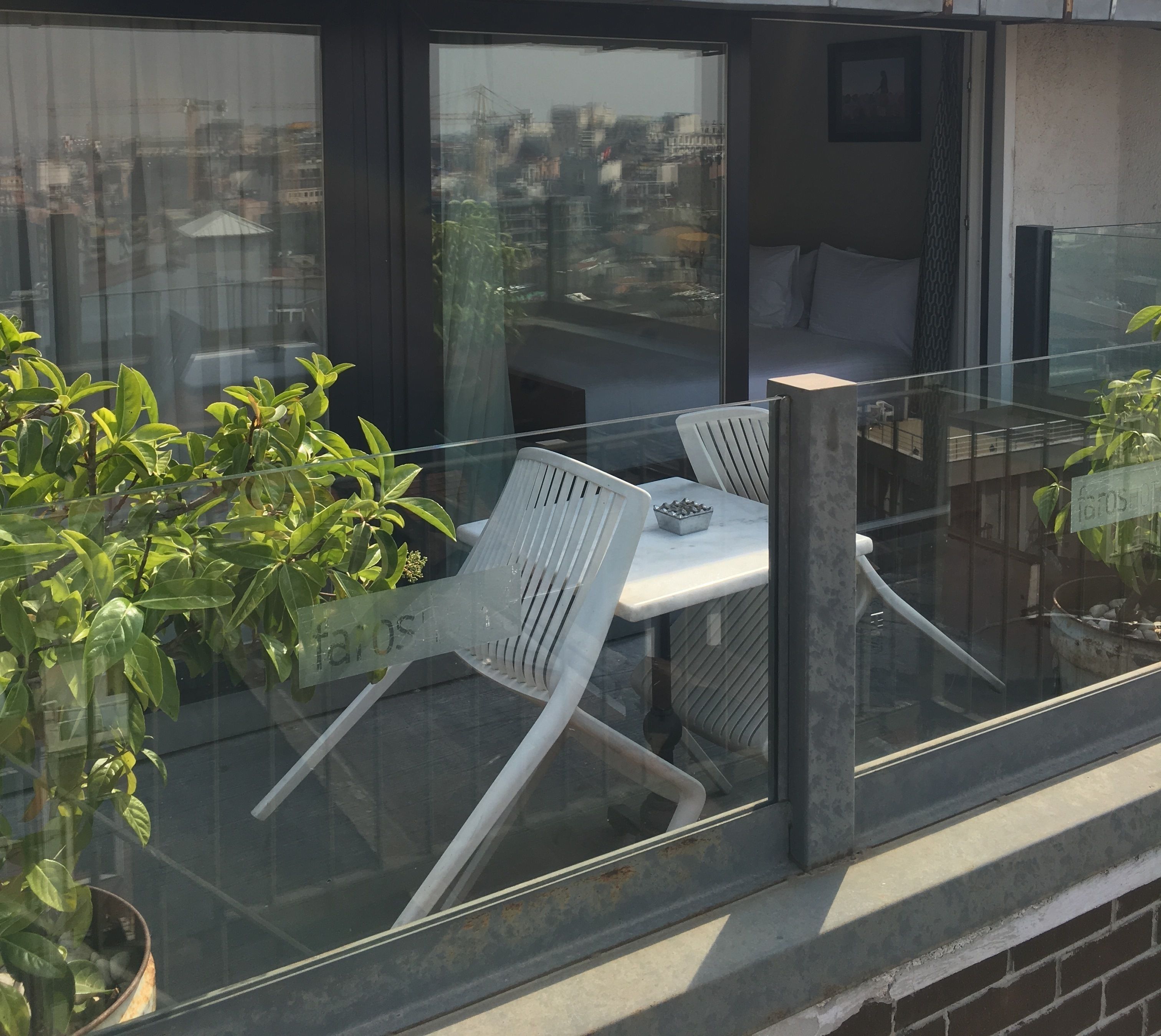 A balcony with a glass railing, two white chairs, a small table, and a potted plant.