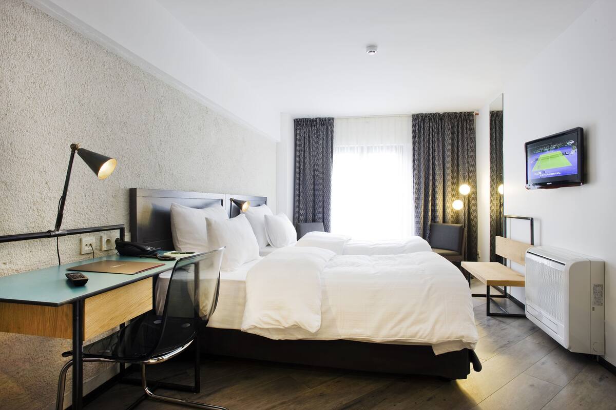 A hotel room with a bed, desk, chair, TV, and a window with curtains.