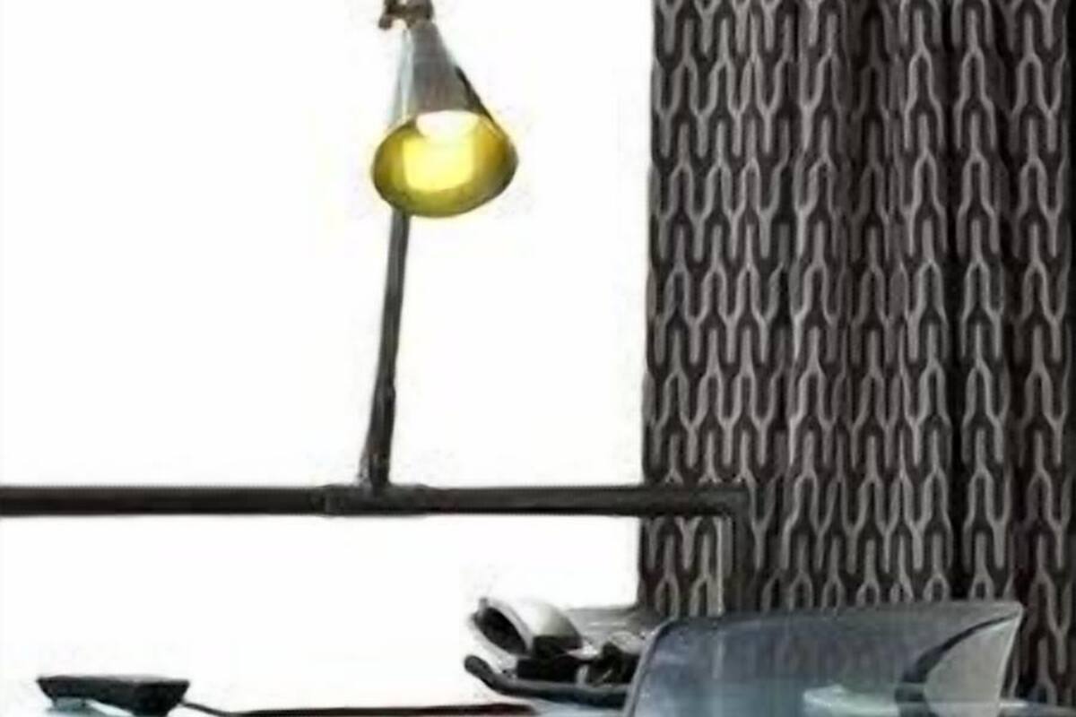A modern hotel room with a desk, chair, lamp, and patterned curtains.