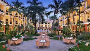 Un patio de hotel con mobiliario exterior, palmeras y una piscina.