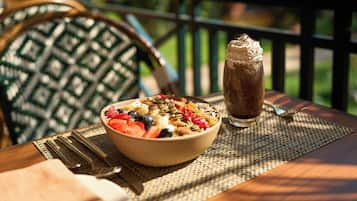 A breakfast setting with a bowl of cereal and a glass of chocolate milk on a table outdoors.