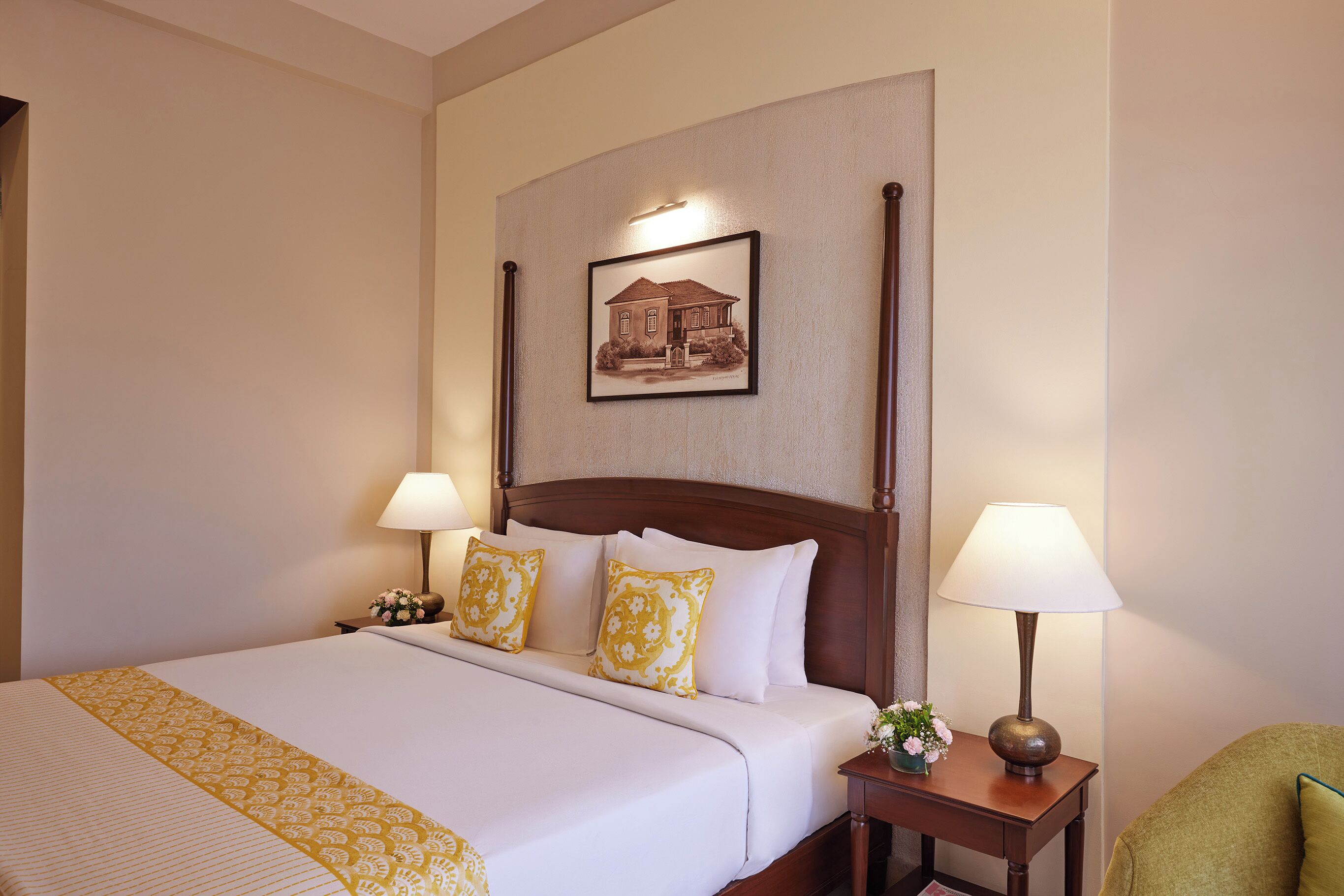 Una habitación de hotel con una cama grande, dos lámparas de noche, una mesita de noche con lámpara y un cuadro enmarcado en la pared.
