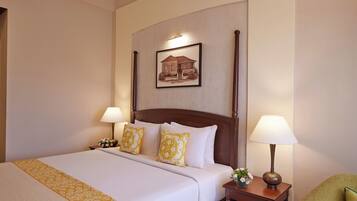 Una habitación de hotel con una cama grande, dos lámparas de noche, una mesita de noche con lámpara y un cuadro enmarcado en la pared.