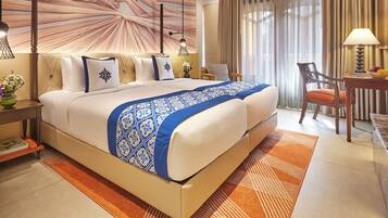 A spacious bedroom with a large bed, a nightstand, a chair, and a desk with a lamp and fruit bowl.