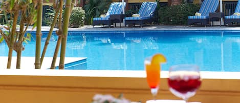 A poolside view with lounge chairs and umbrellas, a glass table with a drink and flowers, and a clear blue pool.