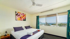 A hotel room with a bed, a ceiling fan, a window with curtains, and a painting on the wall.