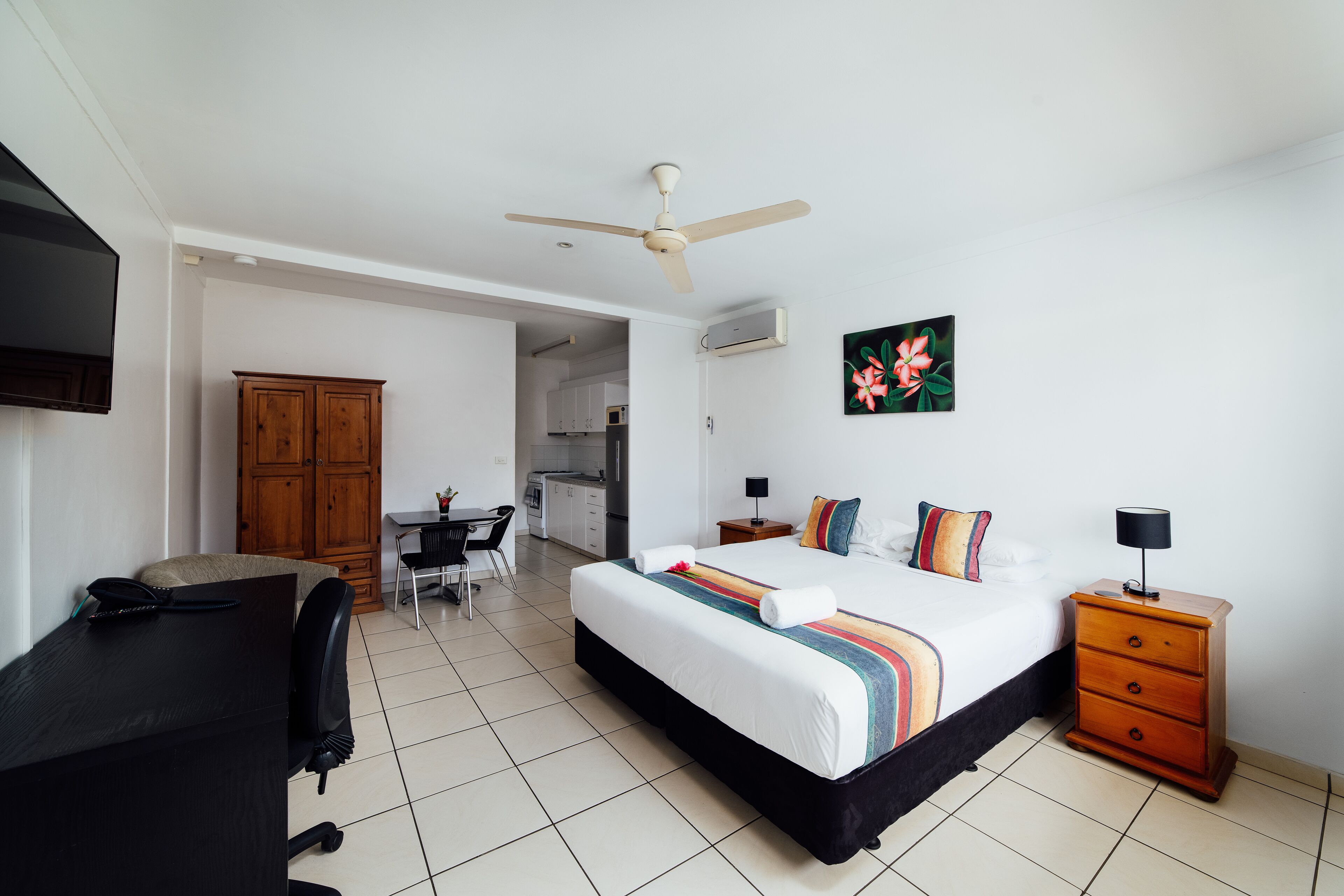Una habitación de hotel con cama, escritorio, silla, armario y ventilador de techo.