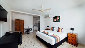 Una habitación de hotel con cama, escritorio, silla, armario y ventilador de techo.
