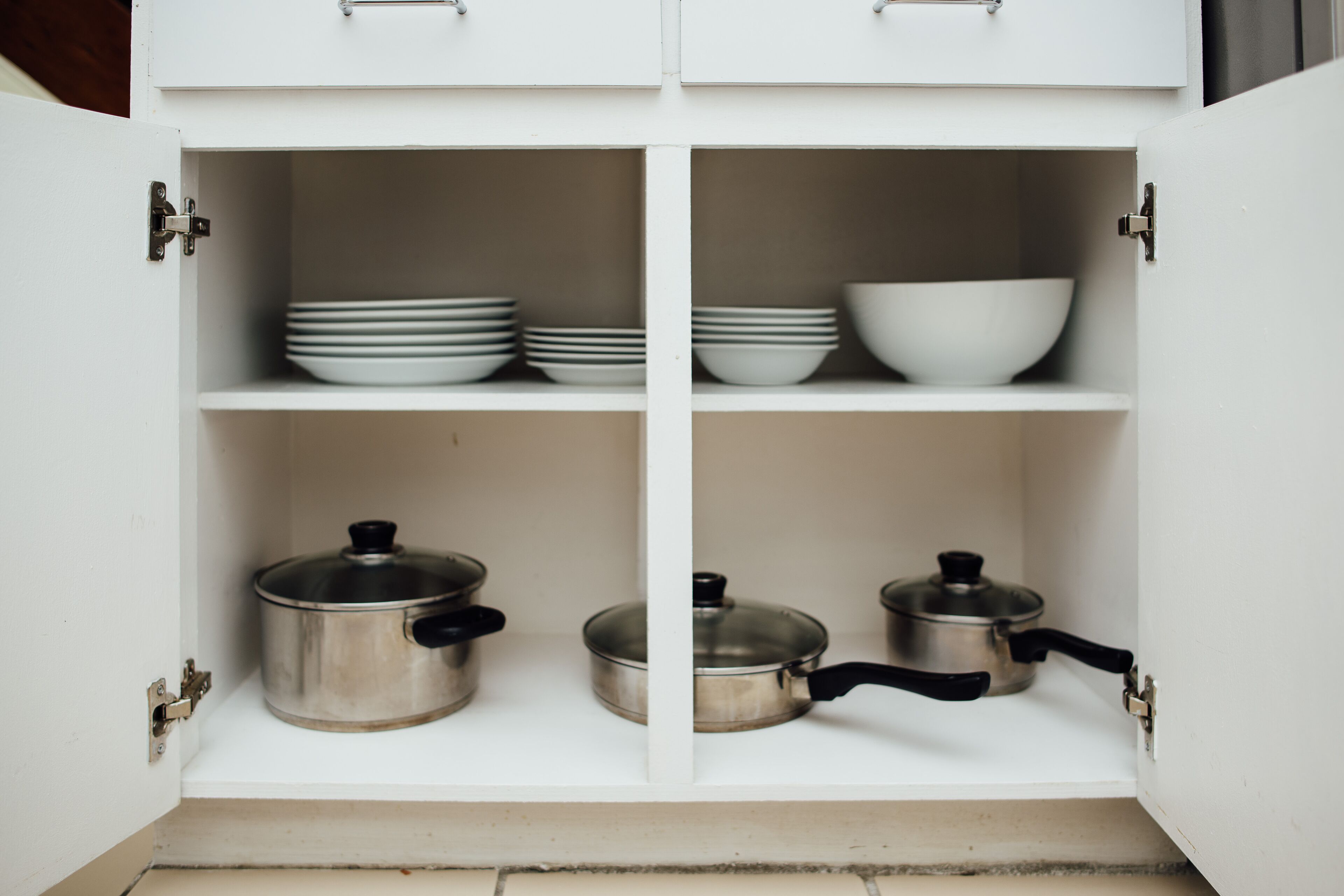 A white kitchen cabinet with four shelves, each containing kitchenware.