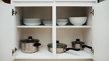 A white kitchen cabinet with four shelves, each containing kitchenware.