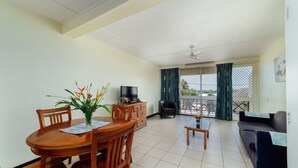 A living room with a dining table, chairs, a sofa, a TV, and a balcony with curtains.