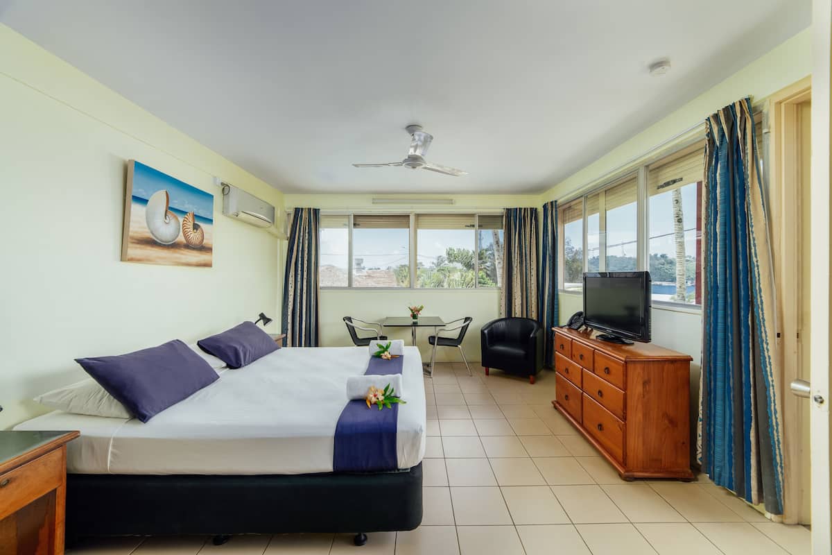 A hotel room with a bed, a desk, a television, a dresser, and a window with curtains.