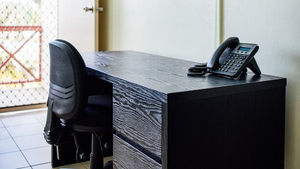 Un espacio de oficina moderno con un escritorio, una silla, un teléfono y un televisor montado.
