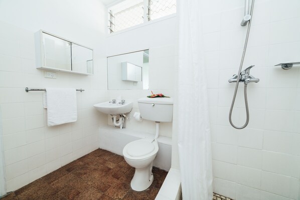 Un baño con azulejos blancos, un inodoro, un lavamanos, una ducha y un espejo.