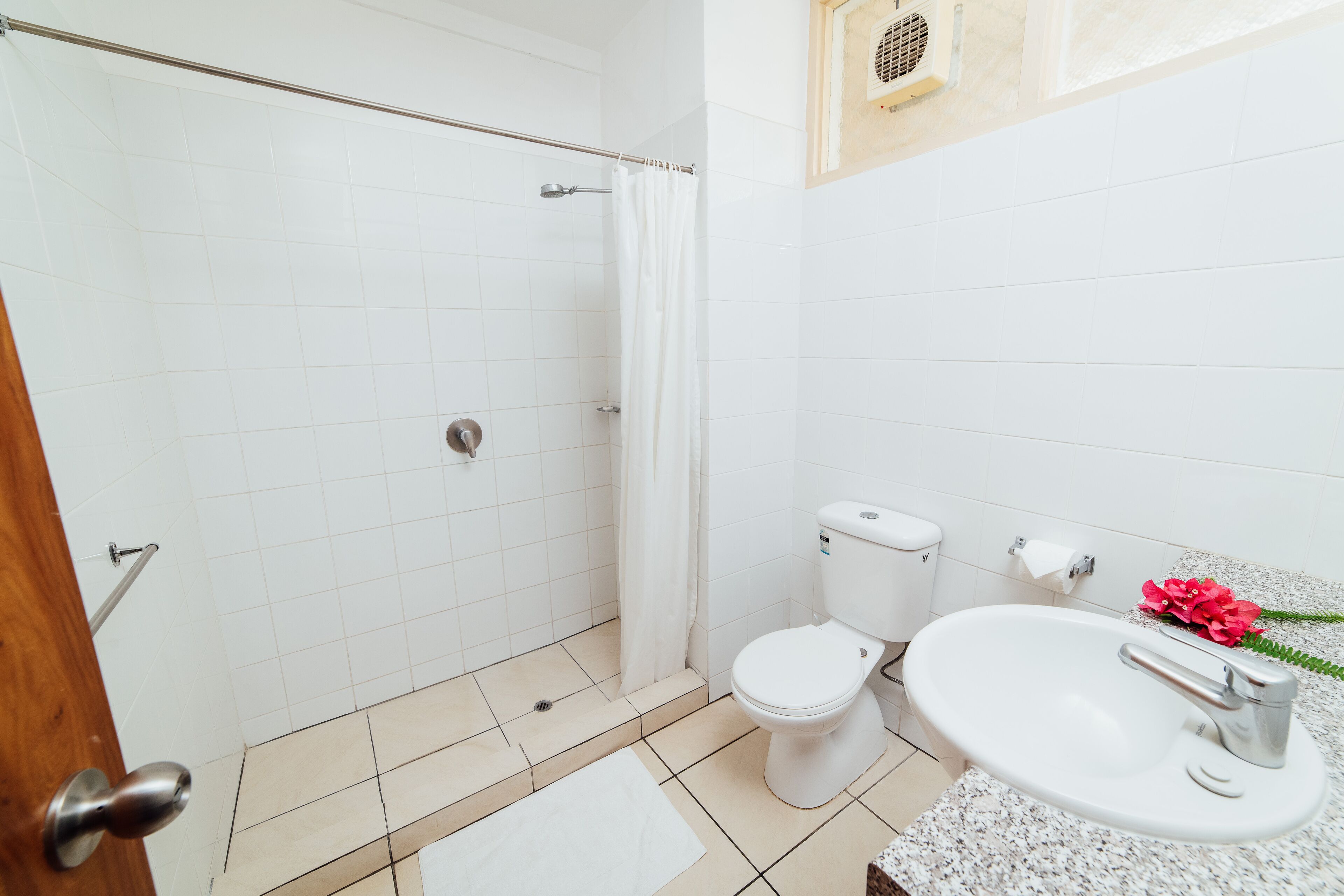 Un baño con ducha, inodoro, lavamanos y un perchero para toallas.